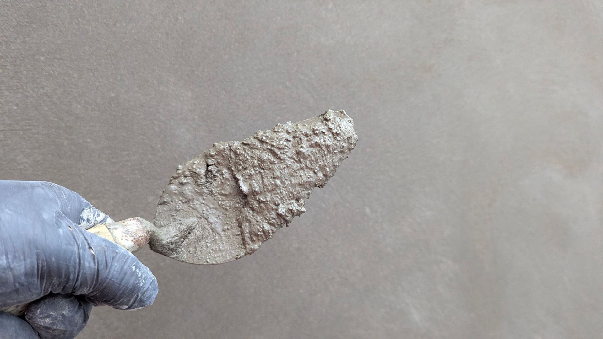 Een troffel met grijs stuc tegen een grijze wand