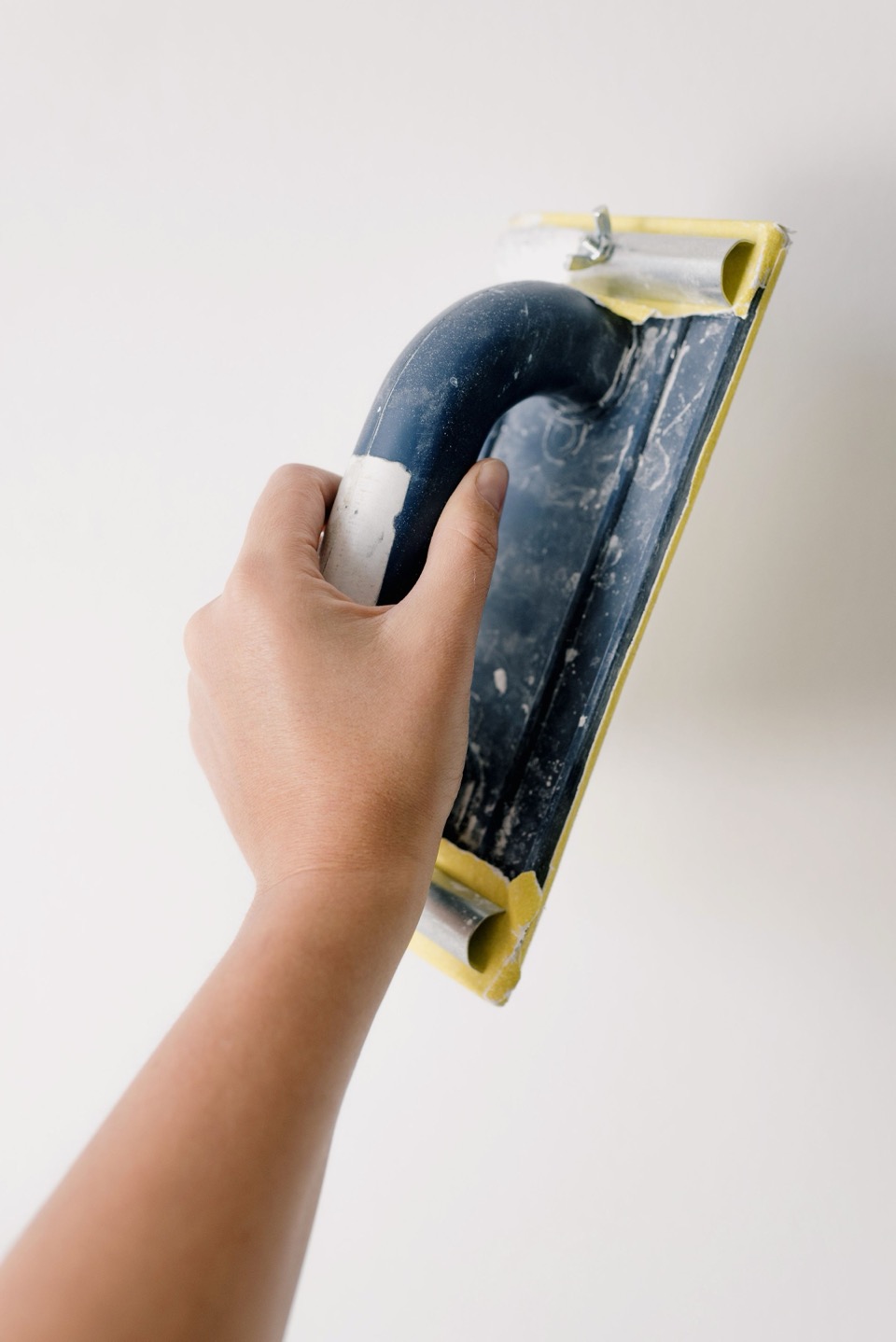 Een hand met een schuurspons werkt een witte muur af